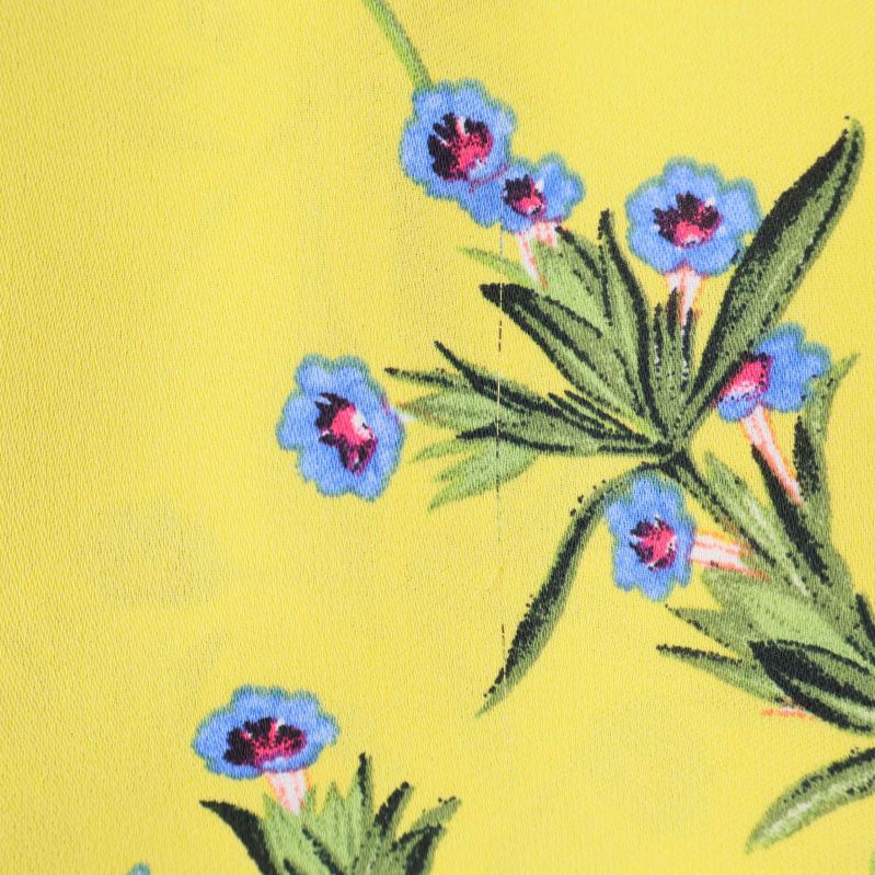 Närbild på blå blommor och grönska mot gul bakgrund
