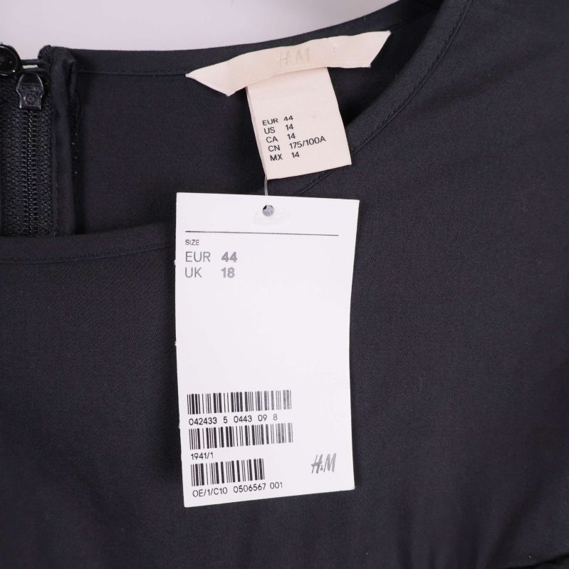 Närbild av klänningens storleksetikett och H&M-tagg