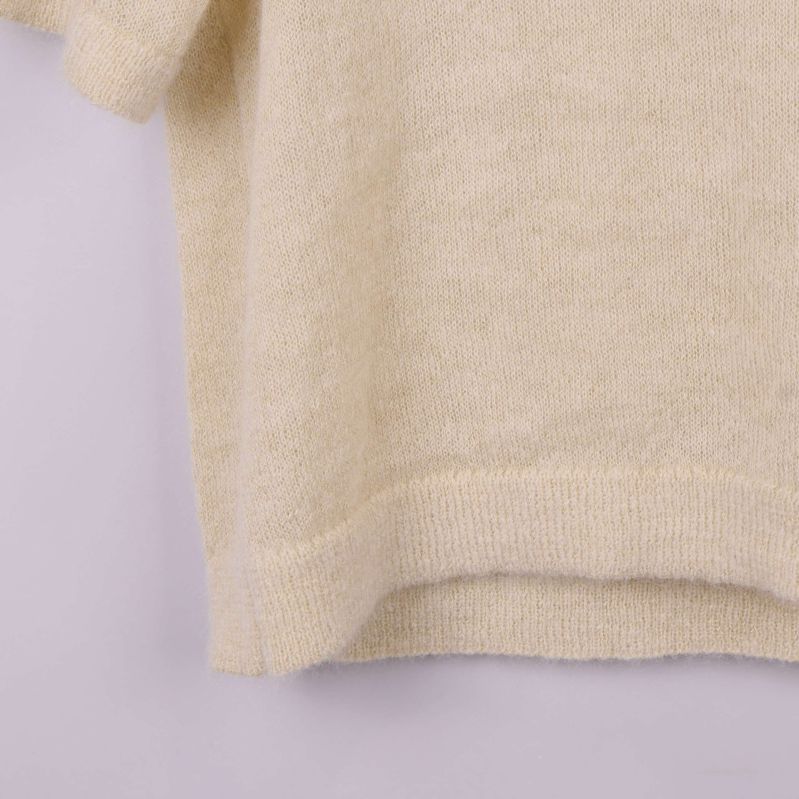 Närbild på nederkanten av beige stickad topp