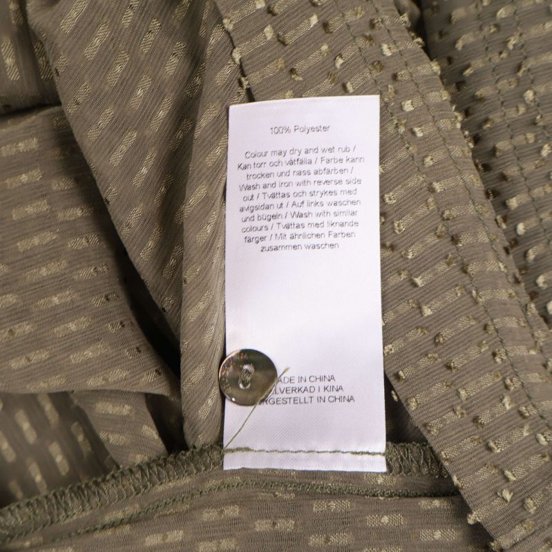 Materiallapp med texten 100% polyester och extra knapp