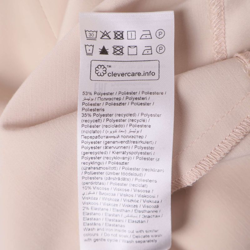 Material- och tvättetikett på beige topp visar polyesterblandning