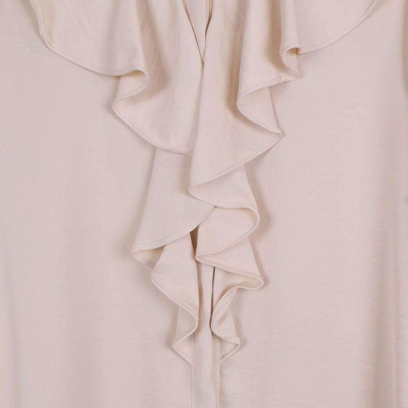 Närbild på volang framtill på beige blus