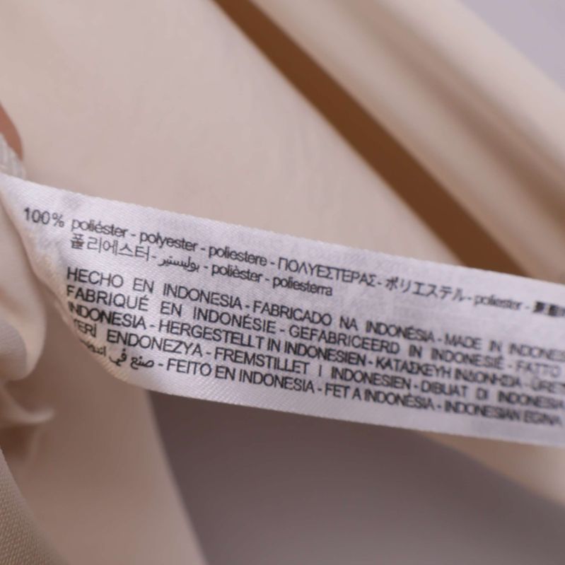 Materiallapp som visar 100 procent polyester på beige blus