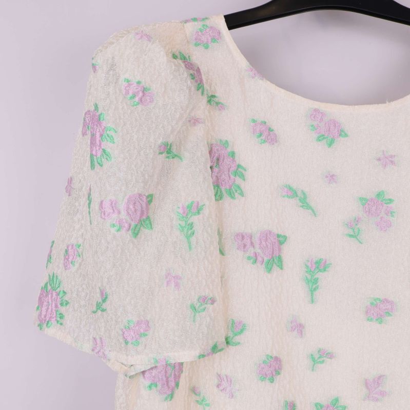 Närbild på puffärm och broderade blommor i lila och grönt