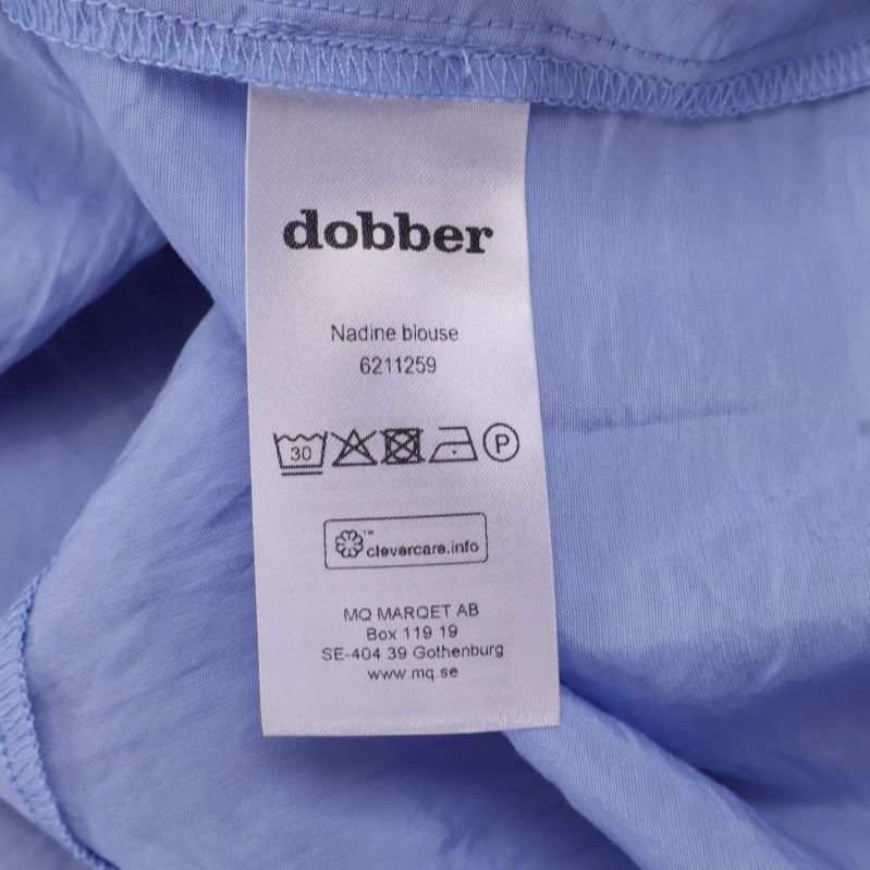 Dobber tvättrådslapp med plaggets namn Nadine bluse
