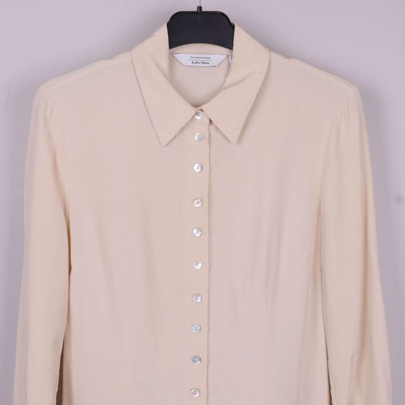 Övre del av beige blus med klassisk krage och knappslå