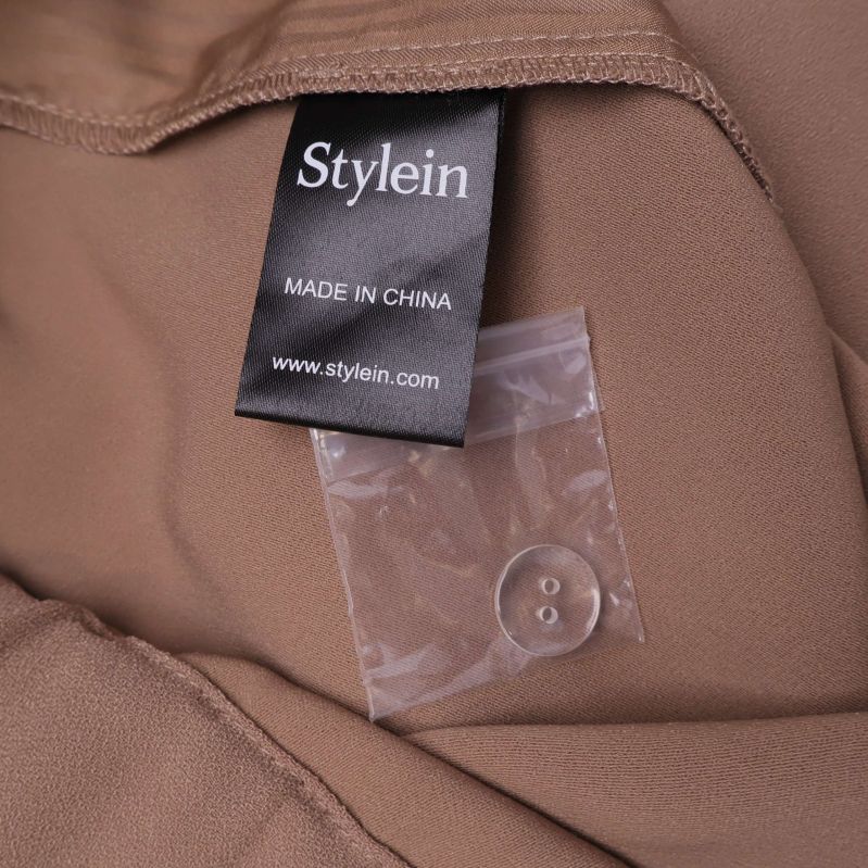Stylein etikett och extra knapp i plastpåse på insidan