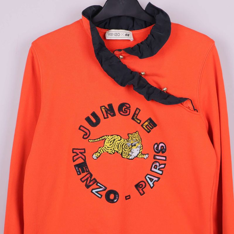Närbild på bröstet av orange sweatshirt med broderad tiger och text