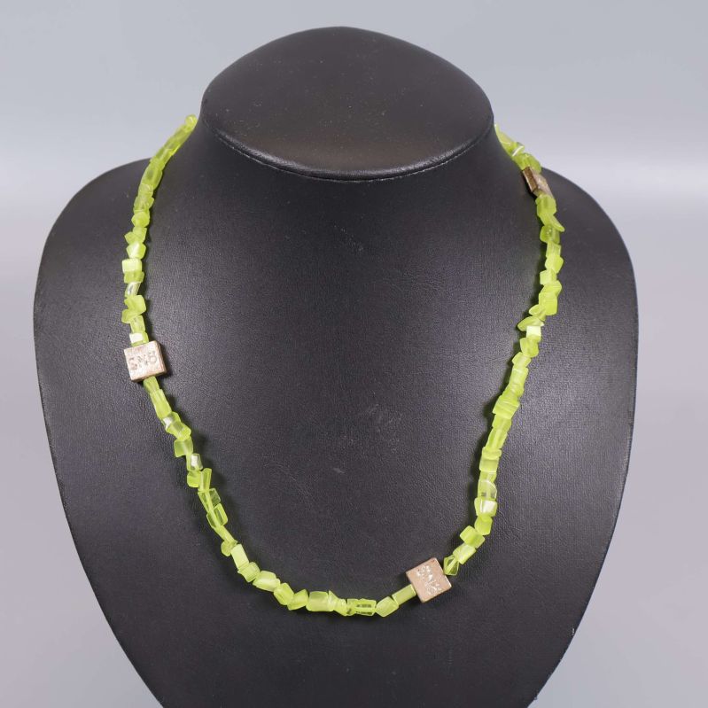 Närbild på limegrönt halsband med gulddetaljer runt displayen