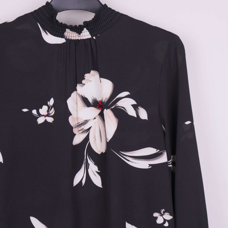 Detaljbild av blomtryck och hög halsringning på blus