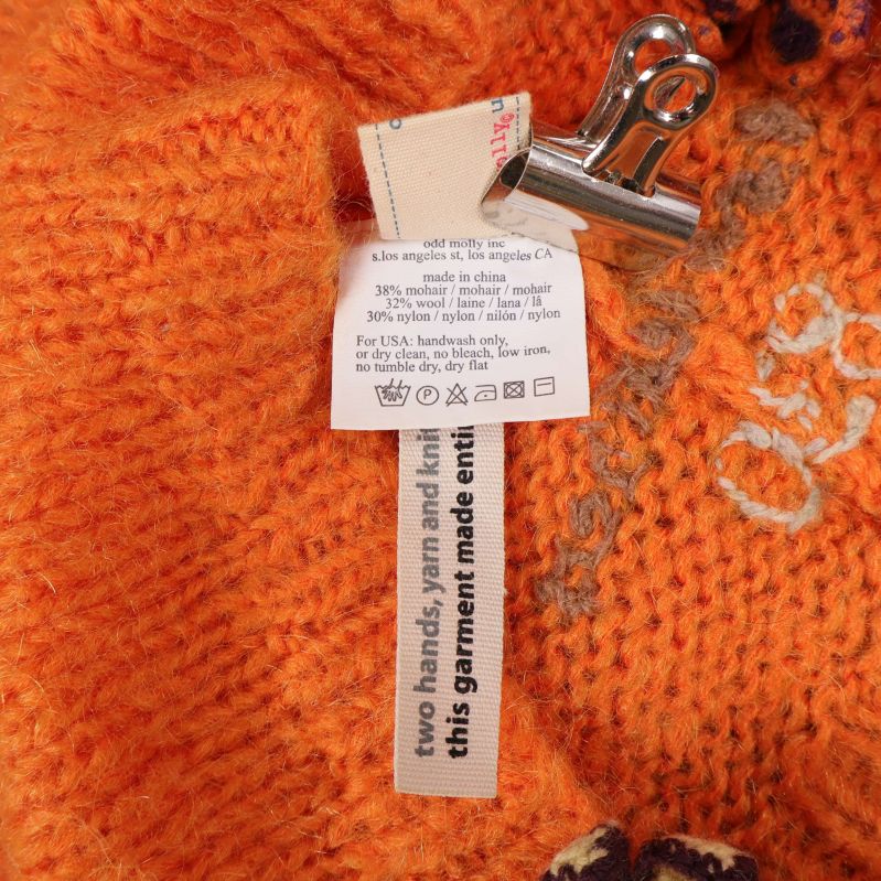 Materiallapp med information insydd i orange stickad mössa