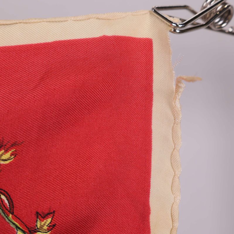 Närbild på vågig gräddvit kant mot röd scarf