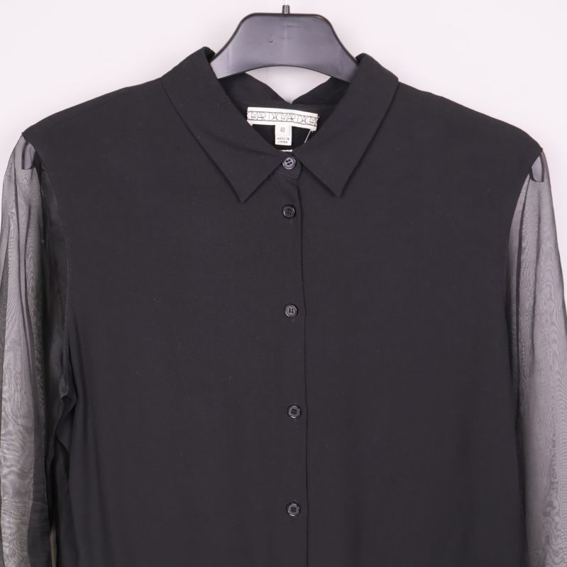 Närbild på krage och knäppning av svart blus med transparenta ärmar