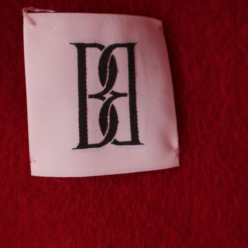 Vit etikett med By Malene Birger monogram på röd poncho