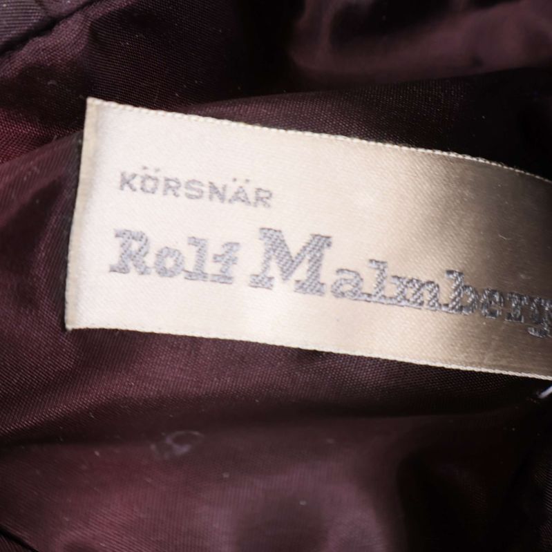 Etikett med texten Körsnär Rolf Malmberg i närbild