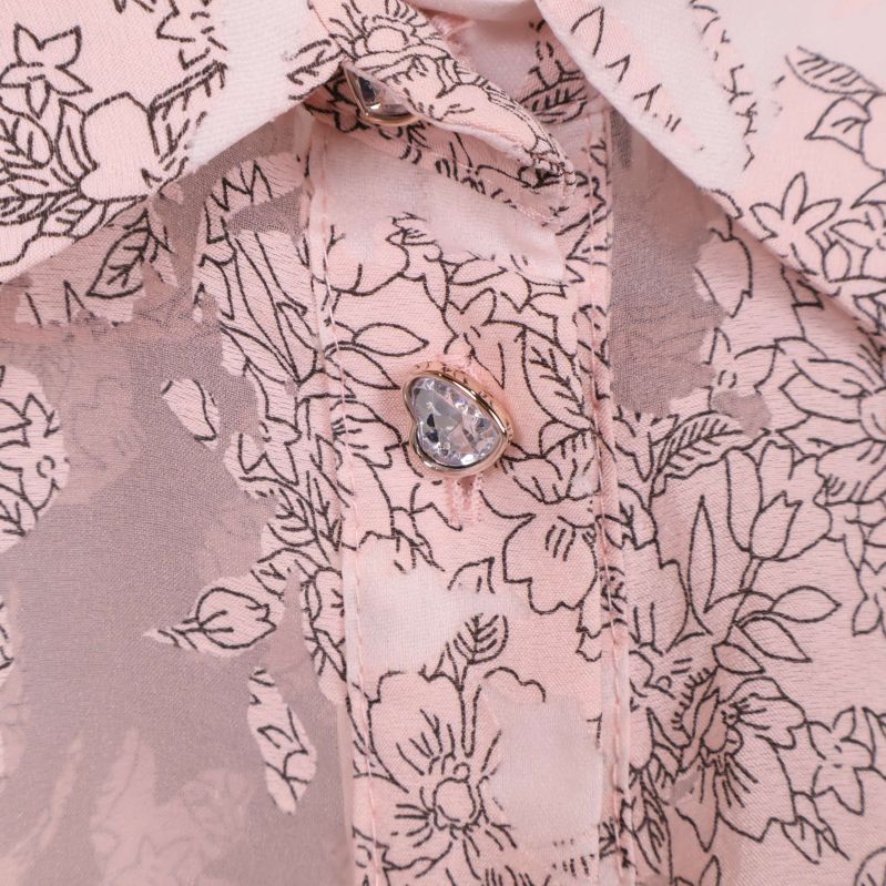 Närbild på knapp och blommönstra detaljer på blus